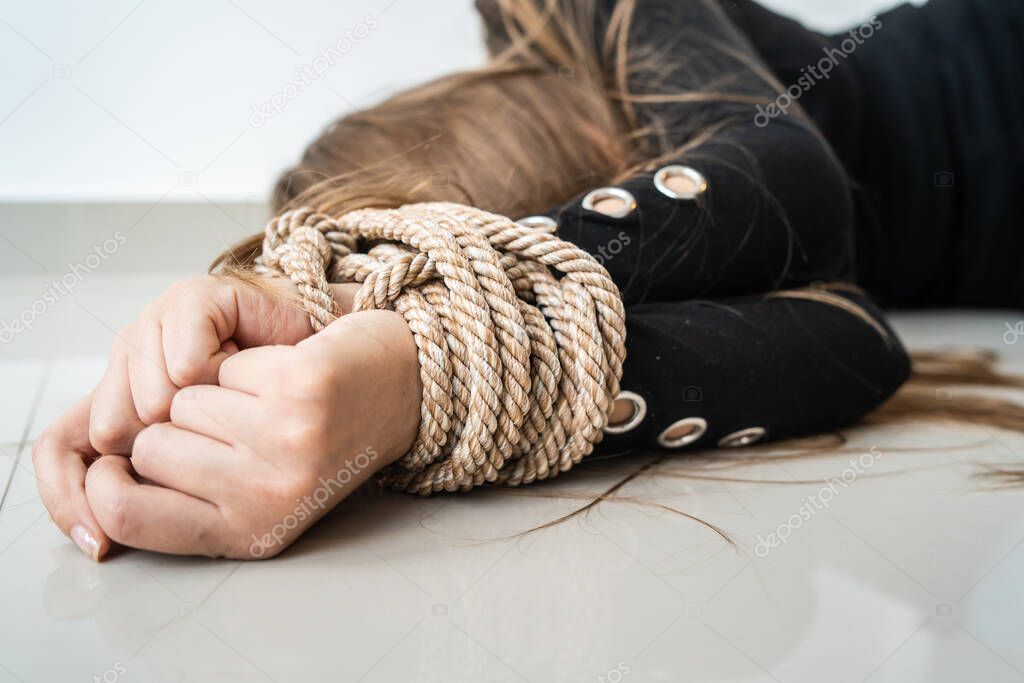 Close up on hands of Unknown caucasian woman or minor girl lying unconsciousness on the floor with rope tied arms - Human rights kidnapping trafficking violence concept selective focus