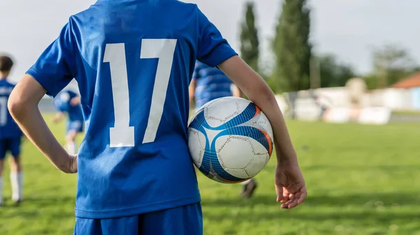 トレーニングやゲーム中に晴れた日にサッカーフィールド上のボールで立って未知の男の子に戻るビュー青の制服を着て 数17コピースペースと — ストック写真