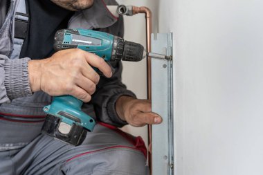 Merkezi ısıtma işleminde metal monte etmek için elektrikli tornavida kullanan kimliği belirsiz beyaz adamın elini kapat.