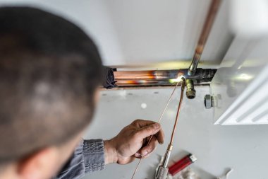Bilinmeyen sanayi işçisi tesisatçı. Merkezi ısıtma bakır boruları olan, evin duvarında meşale ya da kaynak makinesi kullanan, iş yerindeki gerçek insanlar.