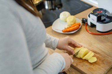 Mutfakta elinde bıçakla bilinmeyen bir kadının omuzlarının üstünden vejetaryen ya da vejetaryen çorbası için patates dilimleri keserken organik sebzelerden sağlıklı yemek pişirirken görülüyor.