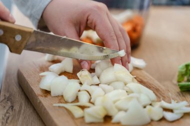 Mutfakta bıçaklı, vejetaryen ya da vejetaryen çorbası için soğan doğrayan organik sebzelerden sağlıklı yemek pişiren kimliği belirsiz bir kadının ellerinde.