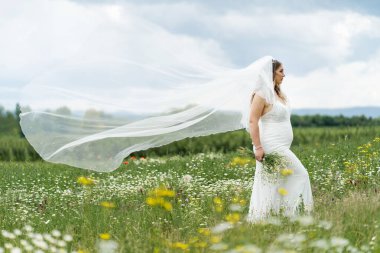 Evlilik kavramı. Bir gelin tarlada tek başına duruyor. Elinde bir buket çiçek var.