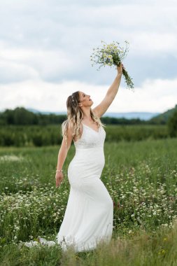 Evlilik kavramı. Bir gelin tarlada tek başına duruyor. Elinde bir buket çiçek var.