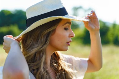 Yan görünüş, yaz günü tarlada şapkalı güzel beyaz kadın portresi. Kapalı hayaller kuruyor.