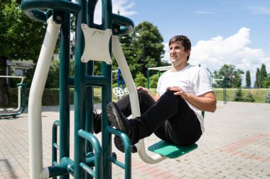 Yetişkin beyaz adam parkta makinede bacak çalıştırıyor. Kendi ağırlığını itiyor. Gerçek insanlar, amatör spor sağlık konsepti.