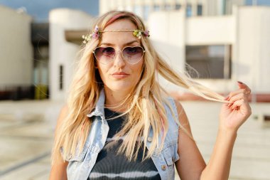 Front view portrait on beautiful caucasian blonde girl with sunglasses in town or city - Pretty blonde woman looking to the camera outdoor in bright summer day - real people concept