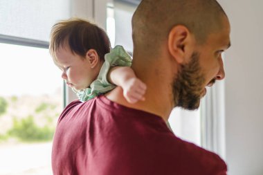 Beyaz bir adam, yaz günü küçük kızını pencerenin önünde tutuyor. Babalar günü konsepti. Gerçek insanlar için.