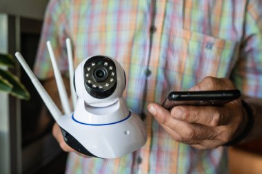 Ev güvenlik kamerası ve cep telefonunu elinde tutan ve bir uygulama ön görünüm kopyalama alanı kurmaya çalışan kimliği belirsiz adamın göbeğini kapatın.