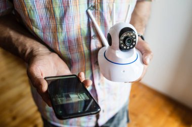 Ev güvenlik kamerası ve cep telefonunu elinde tutan ve bir uygulama üst görünüm kopyalama alanı kurmaya çalışan bilinmeyen adamın orta bölümünü kapatın.