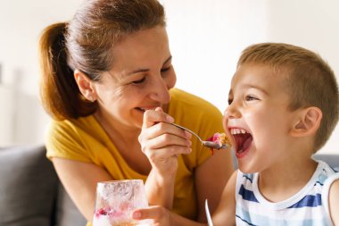 Anne ve yakında evde beslenen beyaz bir kadın kanepeye oturmuş küçük bir çocuğu çöl ile besliyor - yakın plan - ev hayatı neşesi ve çocukluk kavramını bağlayan gerçek insanlar