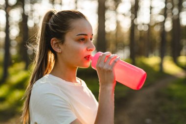 Doğanın ormanlarında, elinde bir şişe su tutarak fren yapan ve doğanın fotokopi alanında dinlenme eğitimi alan beyaz bir kadının yarı uzunluğunda ön manzara.