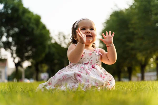 夏または秋の日に畑でドレスを着て草の上に座っている1人の小さな白人の赤ん坊の女の子は 楽しい拍手の手を持って幸せに笑っています 子供時代のコンセプト — ストック写真