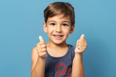 Mavi arka plan stüdyosunun önünde duran dört yaşındaki beyaz çocuk gülümsüyor ve elinde çocuk desteği ve başarı konseptini tutuyor.