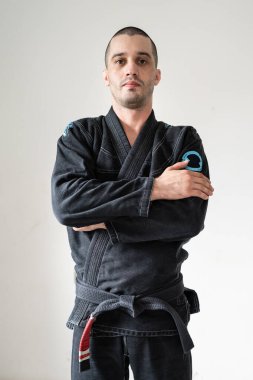 Front view of adult male athlete bjj brazilian jiu jistu black belt standing in front of white wall in kimono gi with looking to the camera clipart