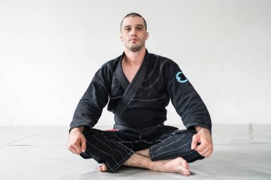 Yetişkin erkek atlet Bjj Brezilyalı jiu jistu siyah kuşak beyaz duvarın önünde kimono gi 'nin içinde fotokopi alanı ile kameraya bakıyor.
