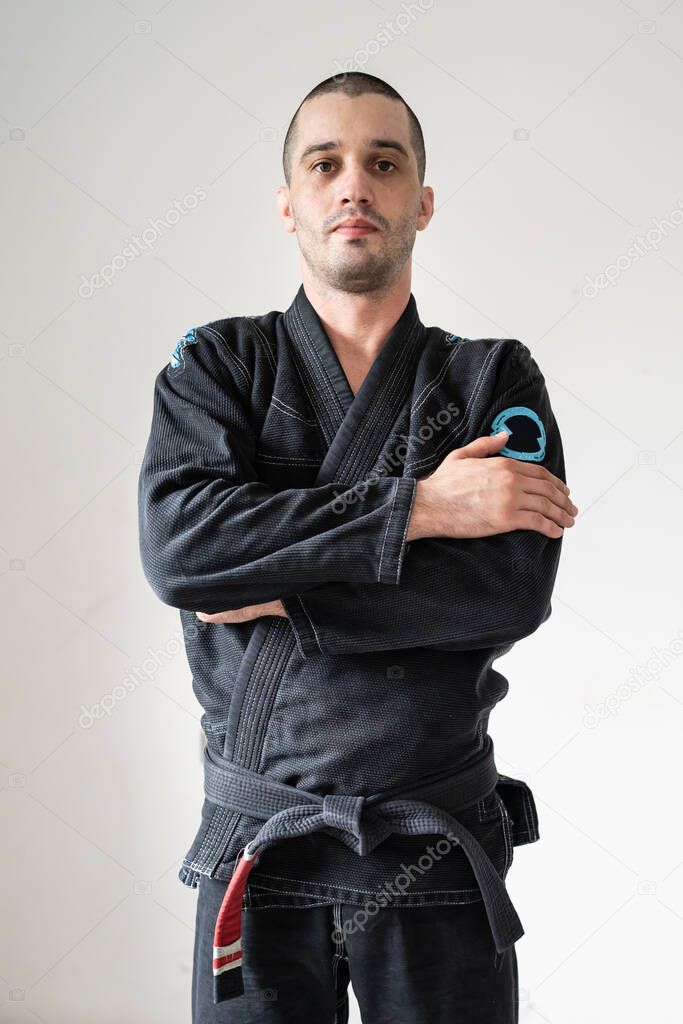 Front view of adult male athlete bjj brazilian jiu jistu black belt standing in front of white wall in kimono gi with looking to the camera