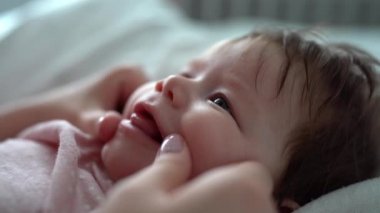Close up portrait of face of small caucasian baby with hand of her mother massaging her gums in order to help her while teeth growing Teething issues at home in day