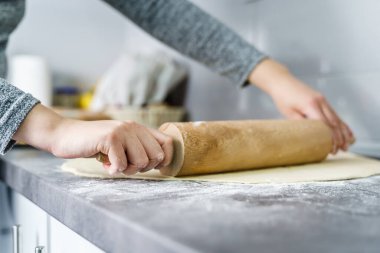 Evdeki mutfak tezgahında merdane kullanarak kruvasana hamur ezmesi hazırlayan kimliği belirsiz beyaz kadının ellerini kapatın. Ev yemekleri ve fırın konsepti.