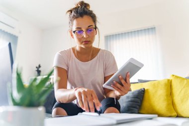 Beyaz kadın Z jenerasyonunun ön görüşü gerçek kripto para birimini araştırıyor. Yatırımdan elde edilen kârı hesaplarken yaz günü kripto para birimlerinde evdeki kanepede oturuyor.