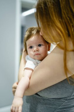 Küçük beyaz bir bebek, dört aylık kızını kucağında tutan annesinin ellerinde.