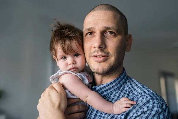 白种人的父亲身穿蓝色衬衫 抱着5个月大的女婴 站在家里的窗边 为人父爱 为人父母 — 图库照片