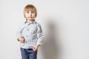 Beyaz duvarın önünde duran küçük sarışın beyaz çocuğun yarım boy portresi. Yanında fotokopi alanı olan küçük çocuk stüdyosu resmi.