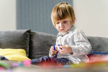Evdeki koltukta mavi kalem tutan küçük beyaz çocuk ya da kız çocuğu portresi el ele tutuşurken açmaya ya da kapatmaya çalışıyor - çocukluk eğlencesi oyun geliştirme konsepti