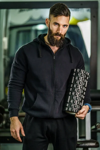 Front view portrait of male athlete standing at gym holding foam massage roller