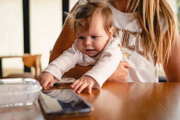Маленька Біла Дитина Руках Матері Намагається Дістатися Мобільного Телефону Столі — стокове фото