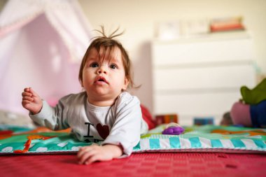 Küçük beyaz kız beş aylık karnının üstüne yatıp yaz günü oyuncak çocukluk konseptiyle oynayıp kameraya tek başına bakıyor.