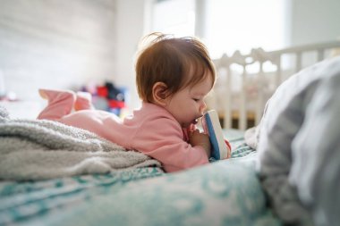 Küçük beyaz bir bebek evde, yatakta tek başına uzanmış elinde kitap oyuncağı olan kameraya bakıyor. Parlak bir çocuklukta oynuyor ve boş zamanlarında büyüyor.