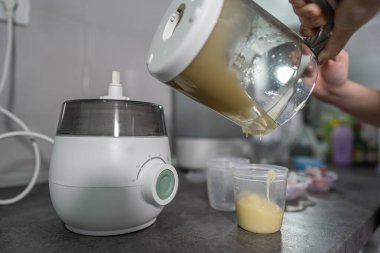 Bilinmeyen bir kadının elinde, mutfak tezgahında saklama için plastik bardağa doldurulmuş patates püresi hazırlarken elektrikli mikserin üzerine yaklaş.