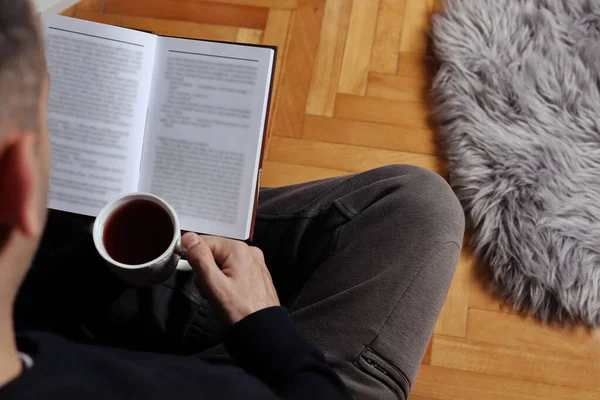Egy Férfi Földön Forró Teát Iszik Otthon Könyvet Olvas Tél — Stock Fotó