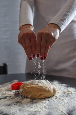 Masadaki kurabiyeler için kadın elleri kurabiye hamuruna un serpiyor. Kadınlar mutfakta tatlı kurabiyeler yapar.