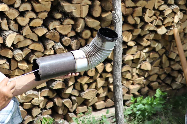 Man cleaning chimney pipe outside with tool. Cleaning a wood burning stove concept. Close up, and wood log in blurred background