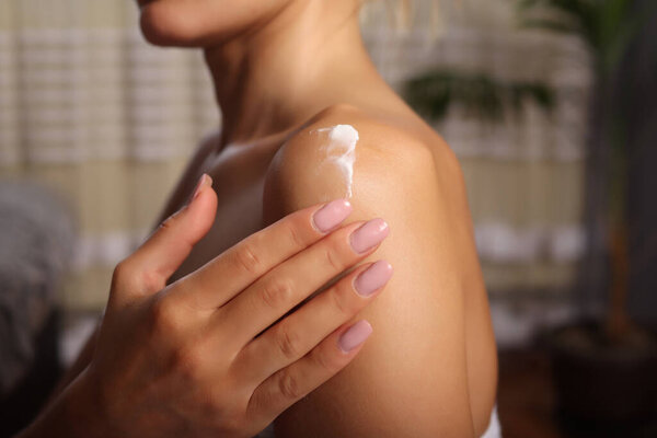Woman with perfect skin in white towel applying cream on shoulder. Advertising of skin moisture and sunscreen product. Skincare and hydration concept