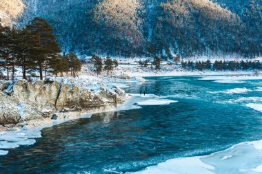 Nehirde kayalar, taşlar ve buzla kaplı kış manzarası. Ağaçlar ve taşlar karla kaplı.