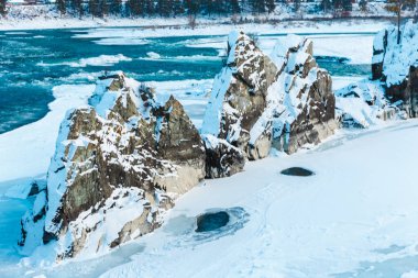 Nehirde kayalar, taşlar ve buzla kaplı kış manzarası. Ağaçlar ve taşlar karla kaplı.