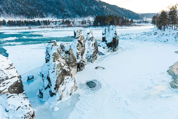 Winter landscape with rocks, stones and ice in the river. The trees and stones are covered with snow