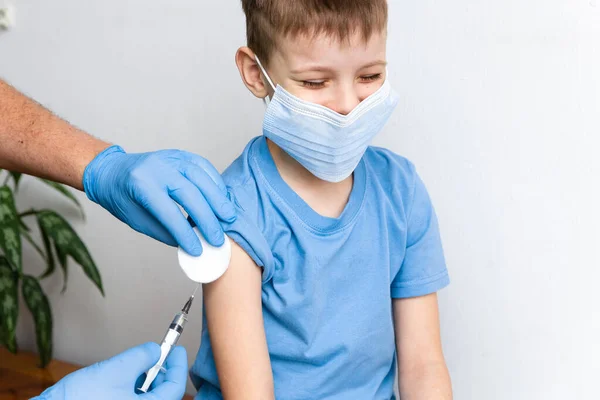 Védőoltás koncepciója. Férfi orvos oltja be a helyes kisfiút a klinikán, közelről. Koronavírus Covid-19 elleni védőoltás és immunitásjavulás Stock Kép
