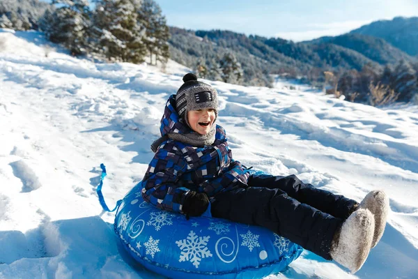 Winter joy and outdoor actovity in snowly forest in mountains. Child boy enjoying tubing ride on snow hill — Stock Photo, Image