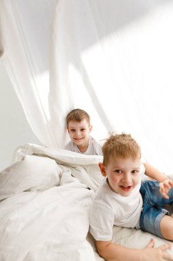 Kapalı alanda pozitif aktivite. Küçük çocuklar yatakta oynuyorlar ve çarşaf kulübesinde eğleniyorlar.