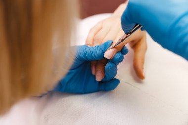 Güzellik salonunda manikür yaptıran genç bir kadın. Manikür, güzellik prosedürleri ve kişisel bakım. Tırnak cilasını kesiyorum. Ellerin yakın görüntüsü