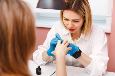 Kadın manikürcü, güzellik salonundaki müşterinin tırnaklarını ojeyle kaplıyor. Manikür, güzellik prosedürleri ve kişisel bakım. Portre