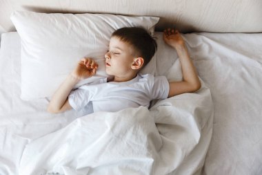 Sevimli küçük çocuk sabah güneş ışığı altında rahat yatağında uyanıyor. Esnemeler ve esnemeler. Günaydın.