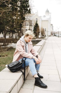 Attractive hipster blonde girl in a pink coat walks around beautiful authentic old town. The concept of freedom. creativity and inspiration