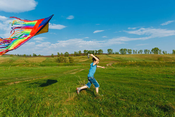 Outdoor activity. Happy boy with a colorful kite running in a meadow in summer in nature and have fun