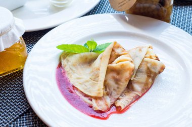 Beyaz tabakta çilek reçelli ince krepler.