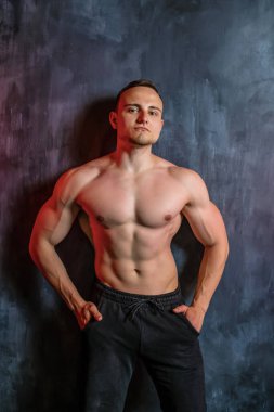 Siyah arka planda fiziğini gösteren genç ve güçlü bir vücut geliştiricinin görüntüsü yakınlarda. Güçlü elleri, karın kasları ve karın kasları olan kendinden emin genç fitness adamı..